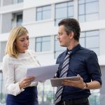 Doi profesionisti analizeaza documentele oficiale ale unei asociatii de proprietari in fata unui bloc modern, servicii de administrare blocuri Bucuresti